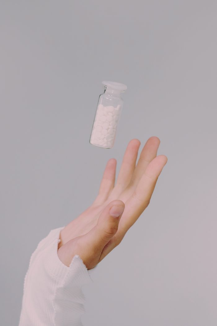 Hand in focus tossing a pill vial against a subtle gray backdrop.