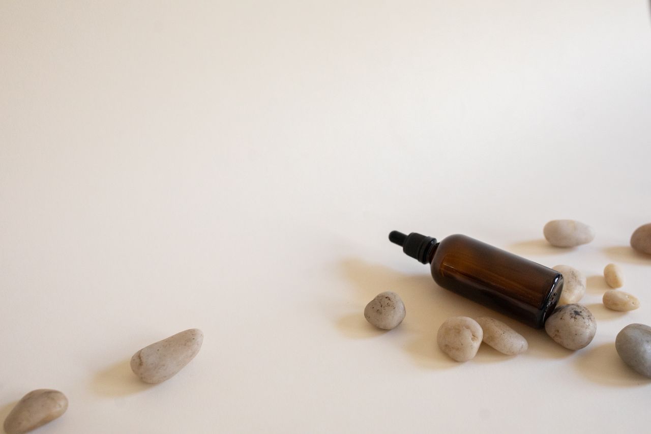 About Essential oil bottle surrounded by smooth stones on a white background, perfect for spa and wellness themes.